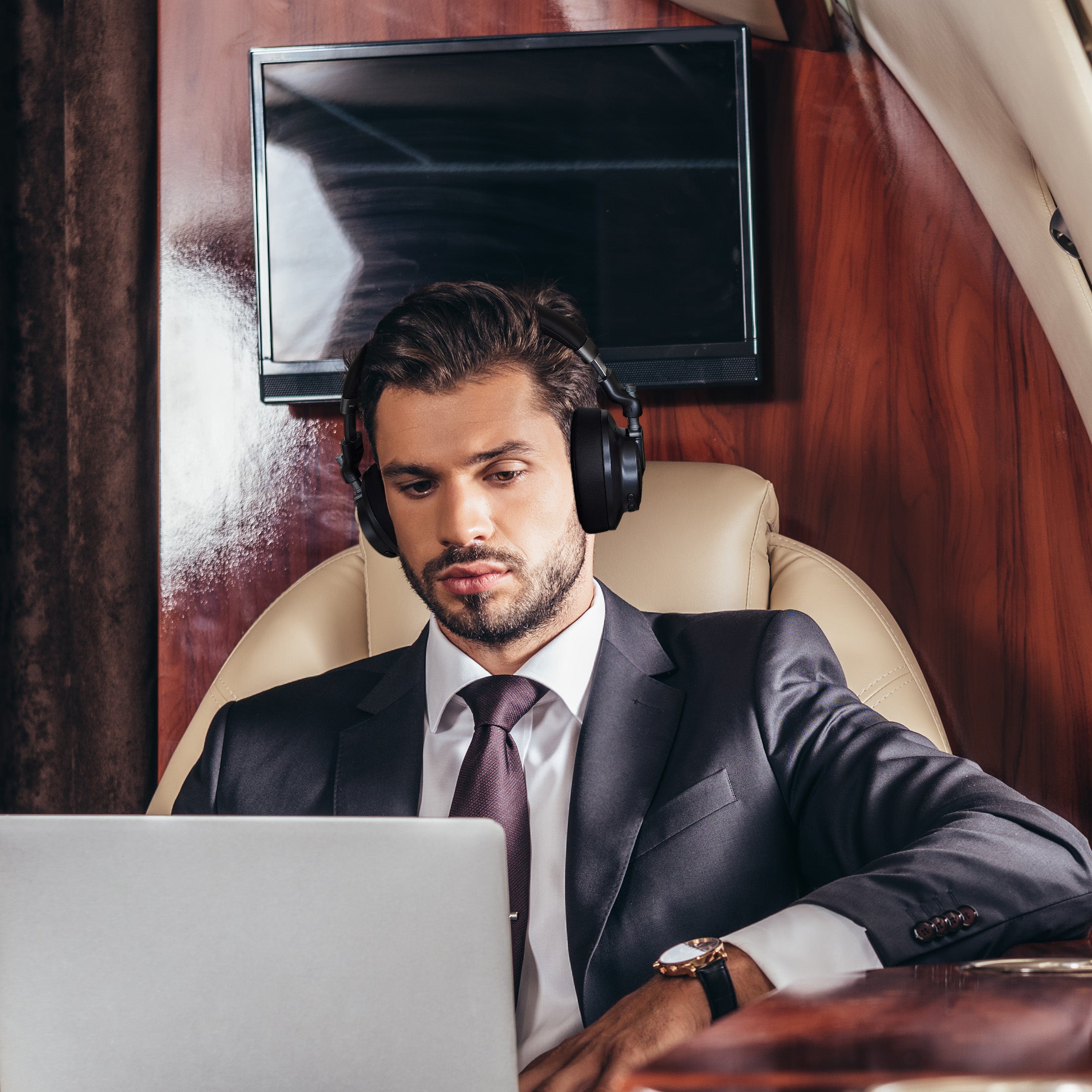 Picture of a business man on an airplane working on his computer with his HP9750HD Verve HD Noise Cancelling Headphones on so he can focus his attention.