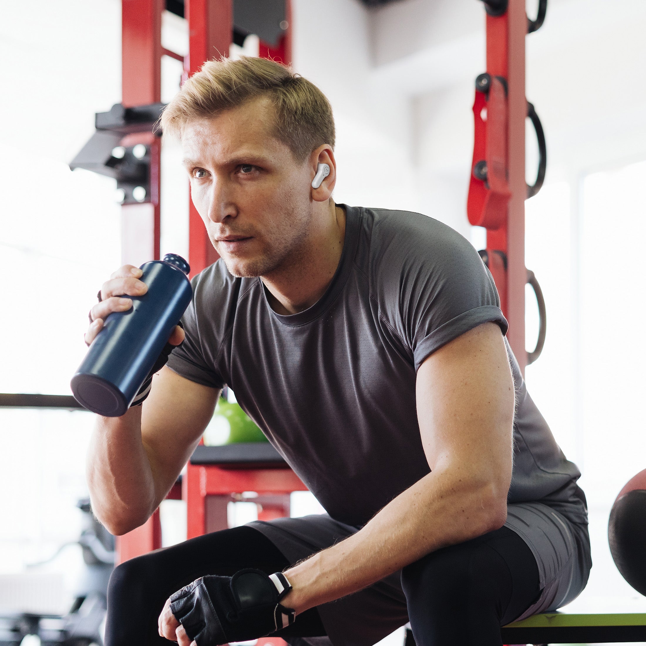Picture of a young fit man at the gym with his Pulse HD Earbuds in and drinking water between workouts.
